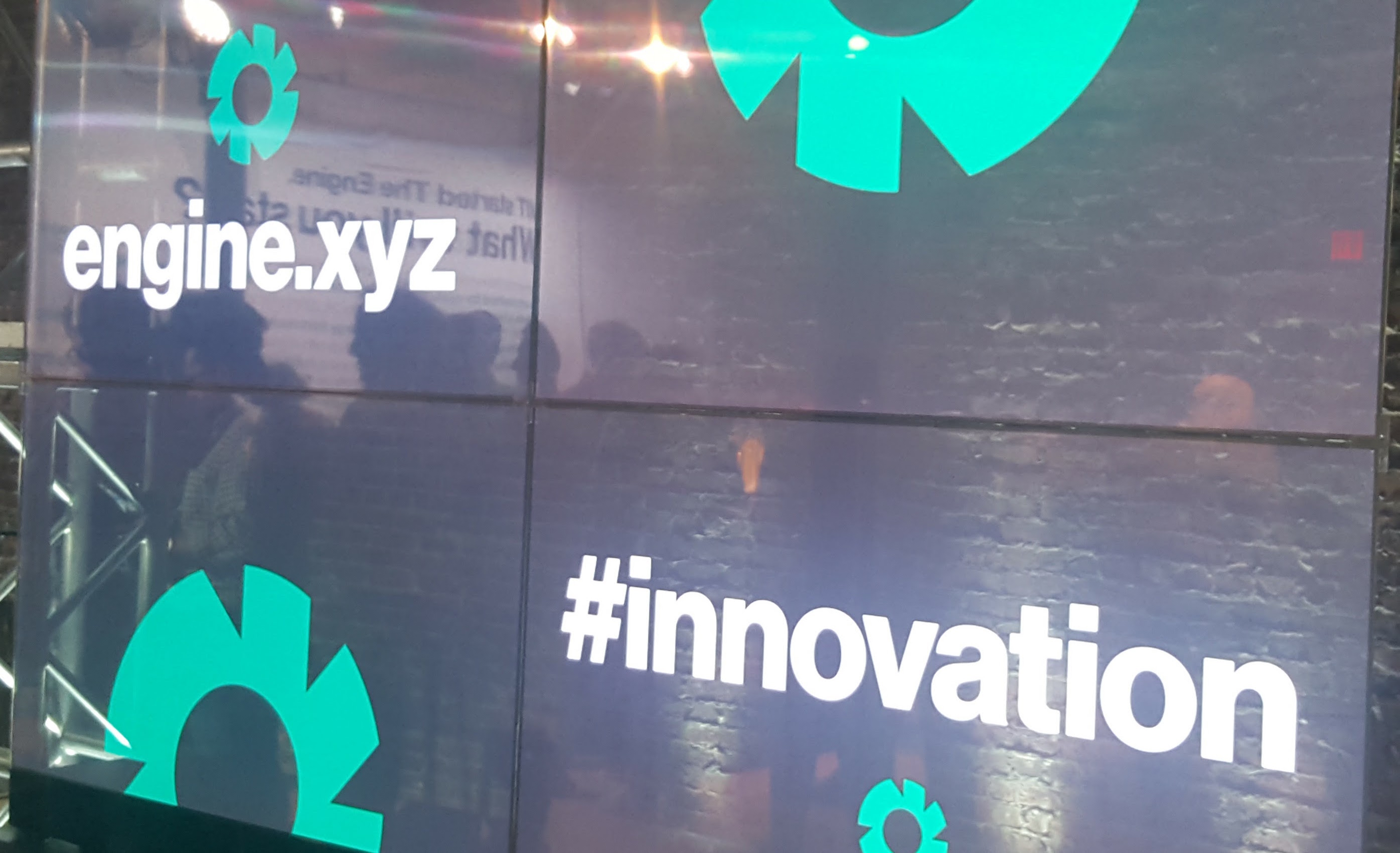 Display wall with The Engine logo in green and engine.xyz and hashtag innovation in white